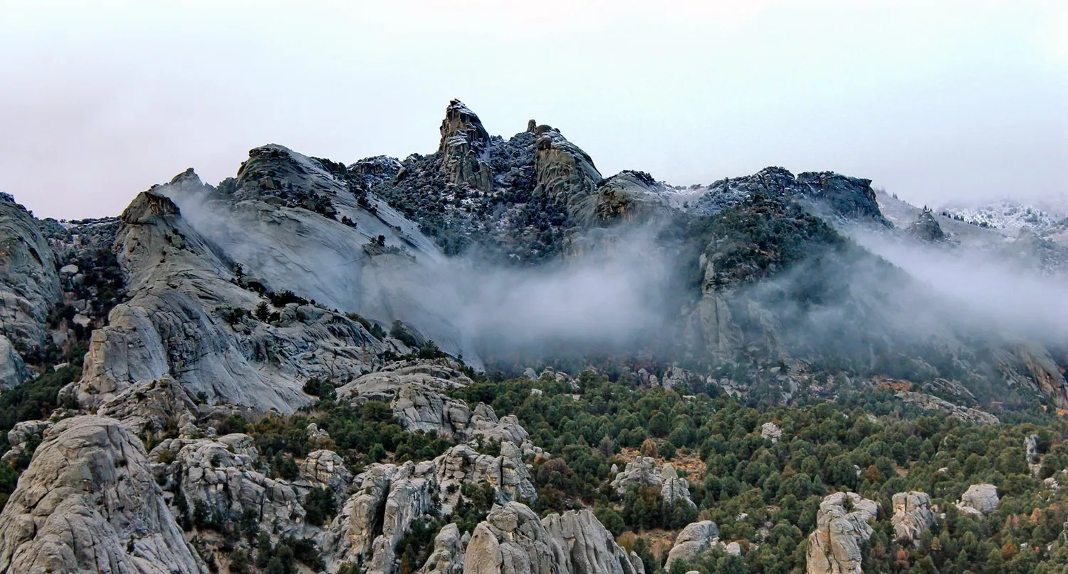 Snow dusted granite formations jut up from a mountainous juniper covered landscape.