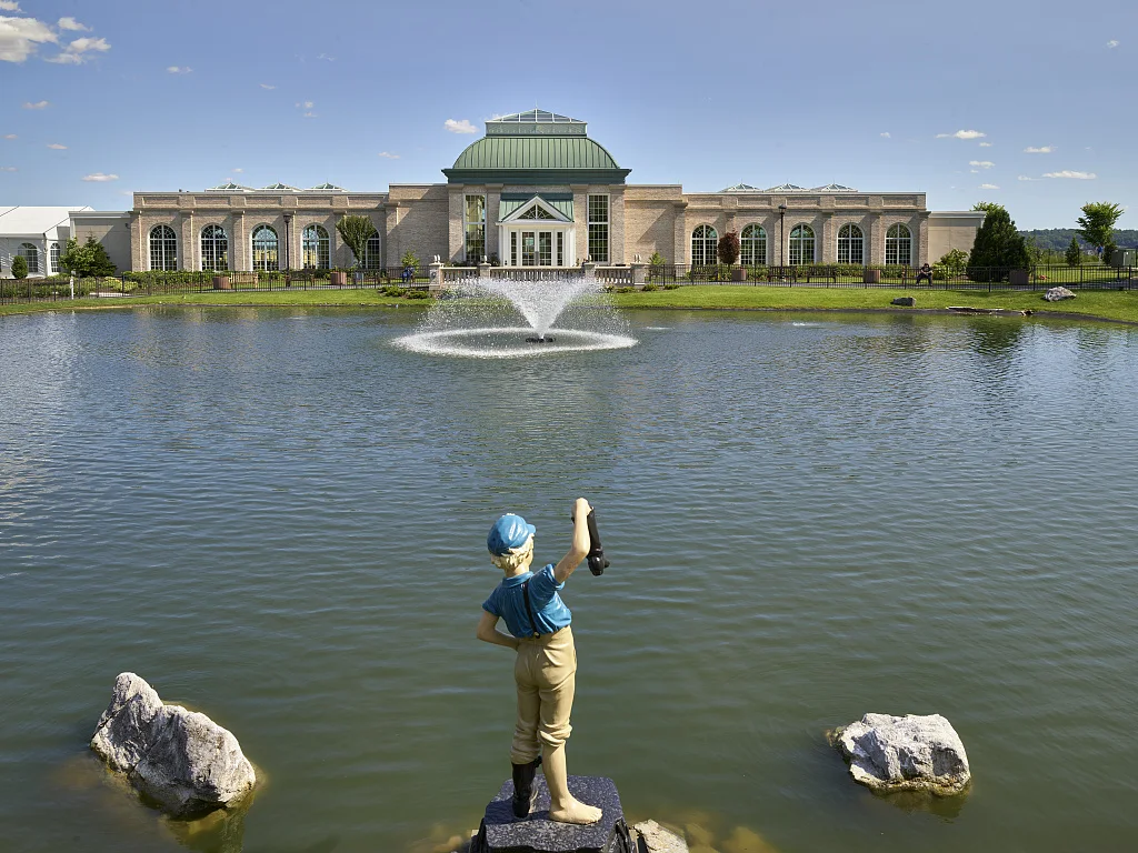 Replica of the Boy with the Leaking Boot statue near the pond and conservatory at Hershey Gardens, a 23-acre botanical display garden, including the conservatory, 3,500 rose bushes, a children's garden, and a butterfly atrium, in Hershey, Pennsylvania. The gardens were opened (at just 3.5 ares) in 1937 by the community's namesake founder, chocolatier Milton S. Hershey. The original, 1913 statue was purchased by Milton and Catherine Hershey for their home
